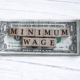 Minimum wage word written on wood block with American Dollar-bills.