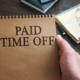 a person holding a notebook with the words paid time off written on it